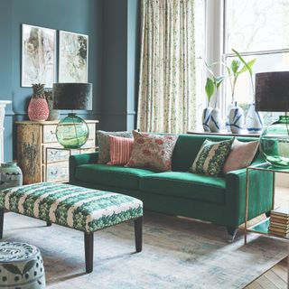 A teal-painted living room with a green sofa and patterned cushions and ottoman