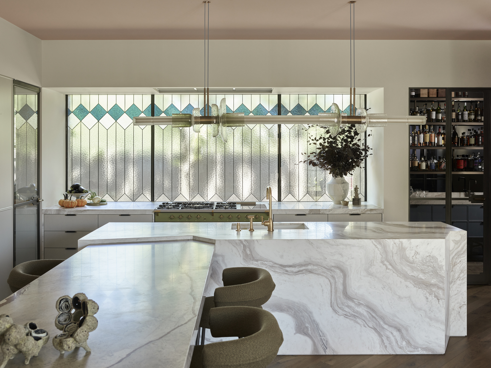 modern kitchen with marble island bench with stained glass windows, pendant light, home bar, and white cabinets