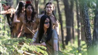 Naru, armed with a bow and arrow, leading her tribe as they walk through a forest