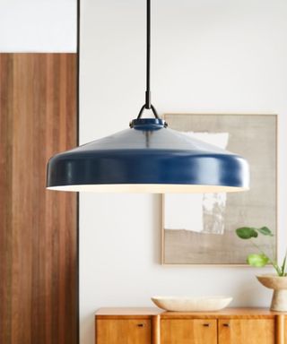 A blue pendant light hanging in front of a room with a wall art print, wooden console table, and door