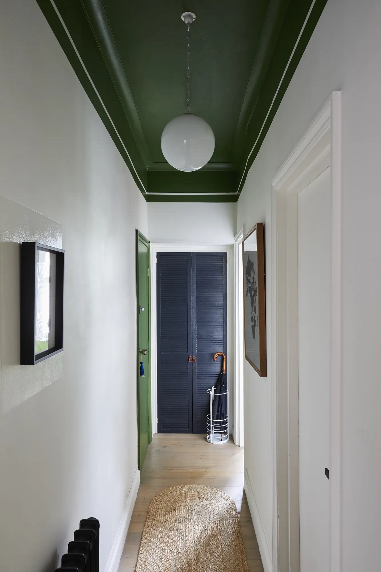 a long hallway with white walls, artworks hanging, a jute rug, and dark green painted ceiling