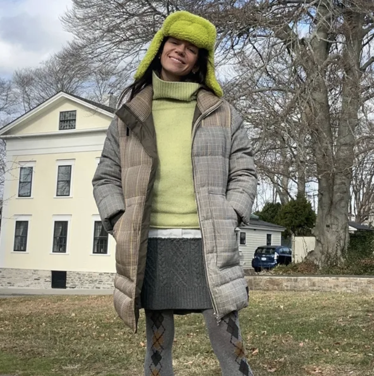 Julia Gall wearing a green hat, a green sweater, a beige coat, and a gray skirt