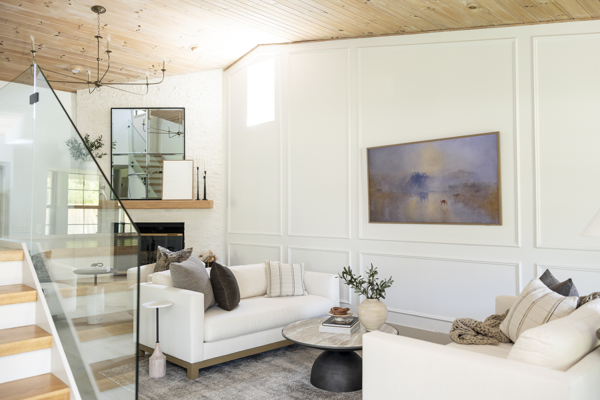 A white-themed living room with wainscoting on the walls, and two white sofas facing each other