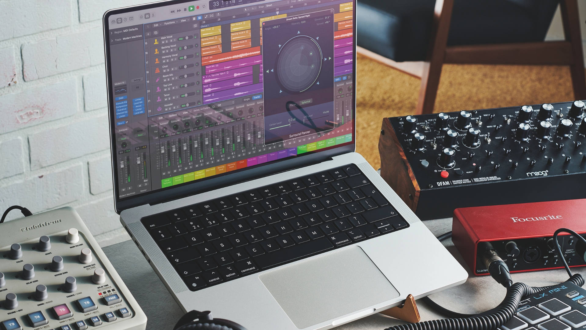 A MacBook Pro on a stand with various music gear in the background