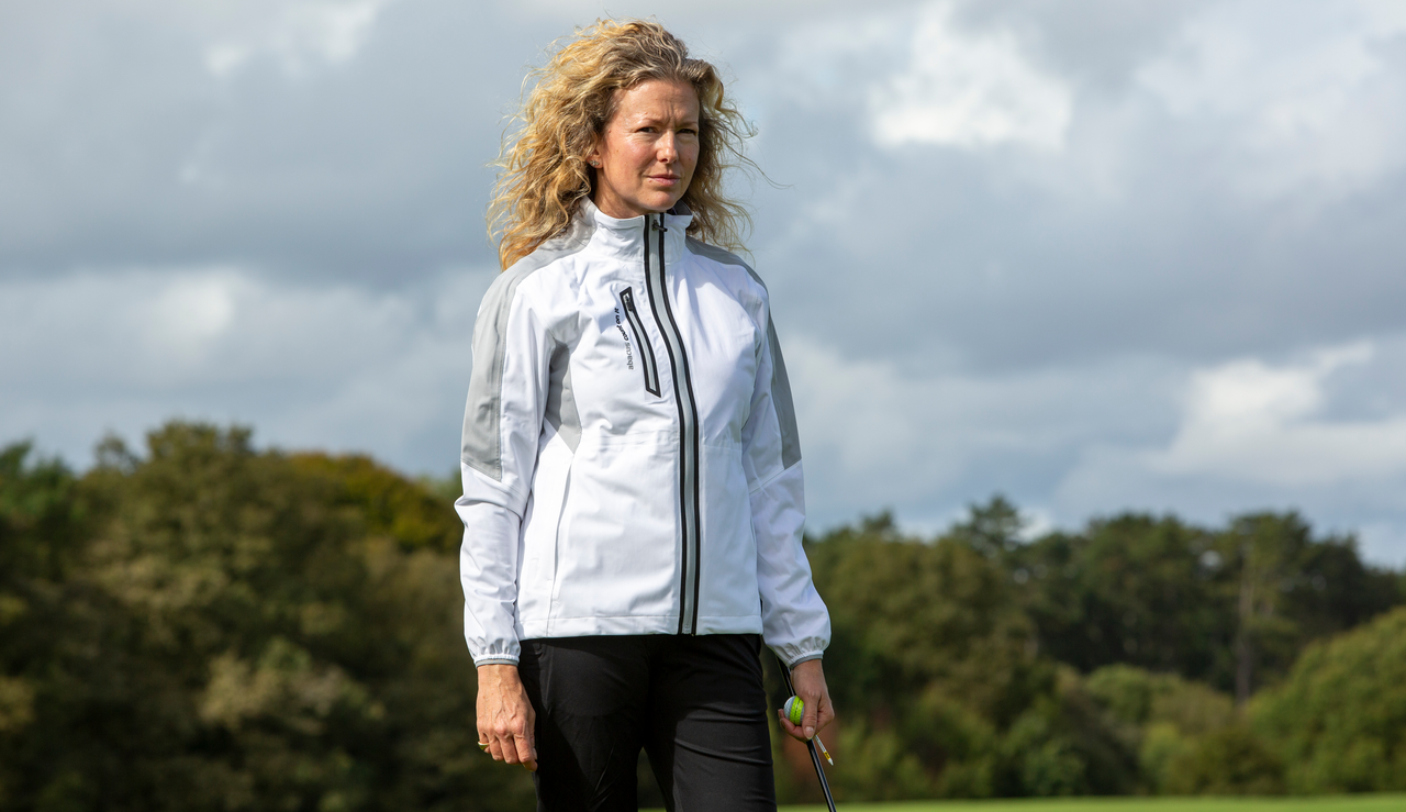 A golfer wears the Abacus Women&#039;s Bounce Rain Jacket in white 