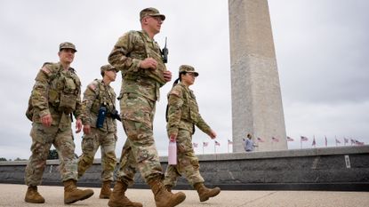 The Washington Monument is visible as National Guard troops walk along the National Mall