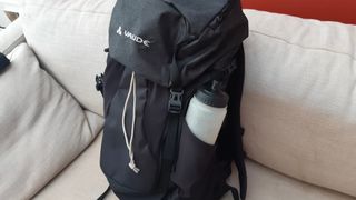 Vaude Brenta 30 backpack on a couch with a water bottle in the side pocket