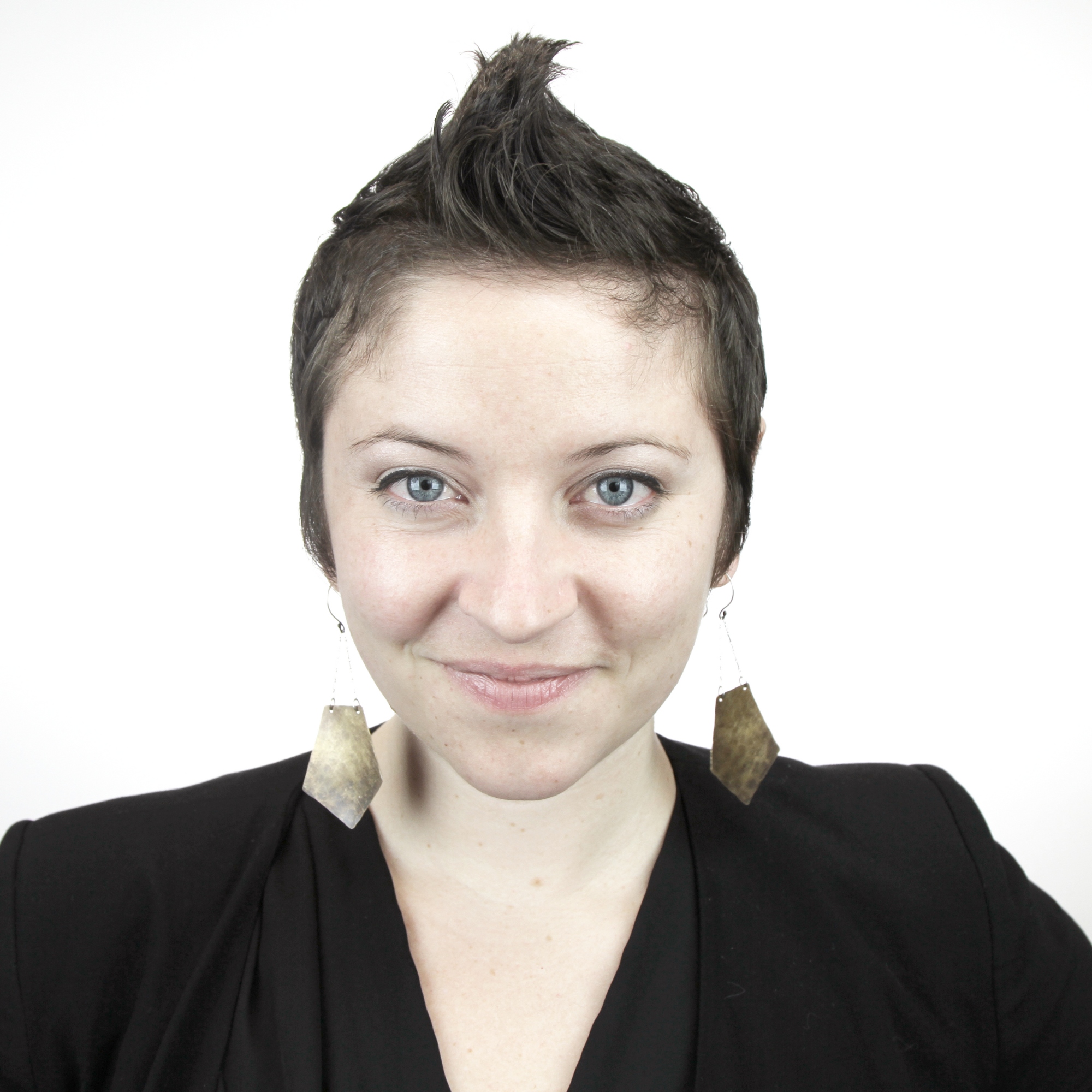 Nisha has short dark hair styled in a quiff and is pictured smiling in a black blouse against white background