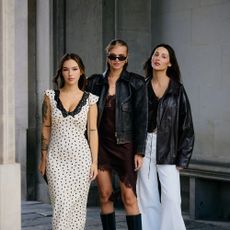 One woman wears a white dress with polka dots. The middle wears a lace trim dress with asymmetric hem, leather jacket, and tall boots. The last wears oversized leather jacket and pants. 