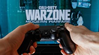 Hands holding PS4 controller in front of screen with Call of Duty: Warzone