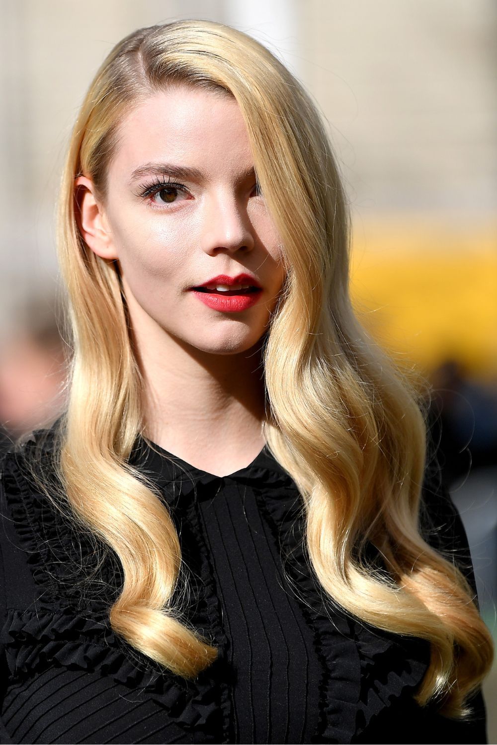 Anna Taylor-Joy on a red carpet wearing a black dress with her hair worn with a deep side parting