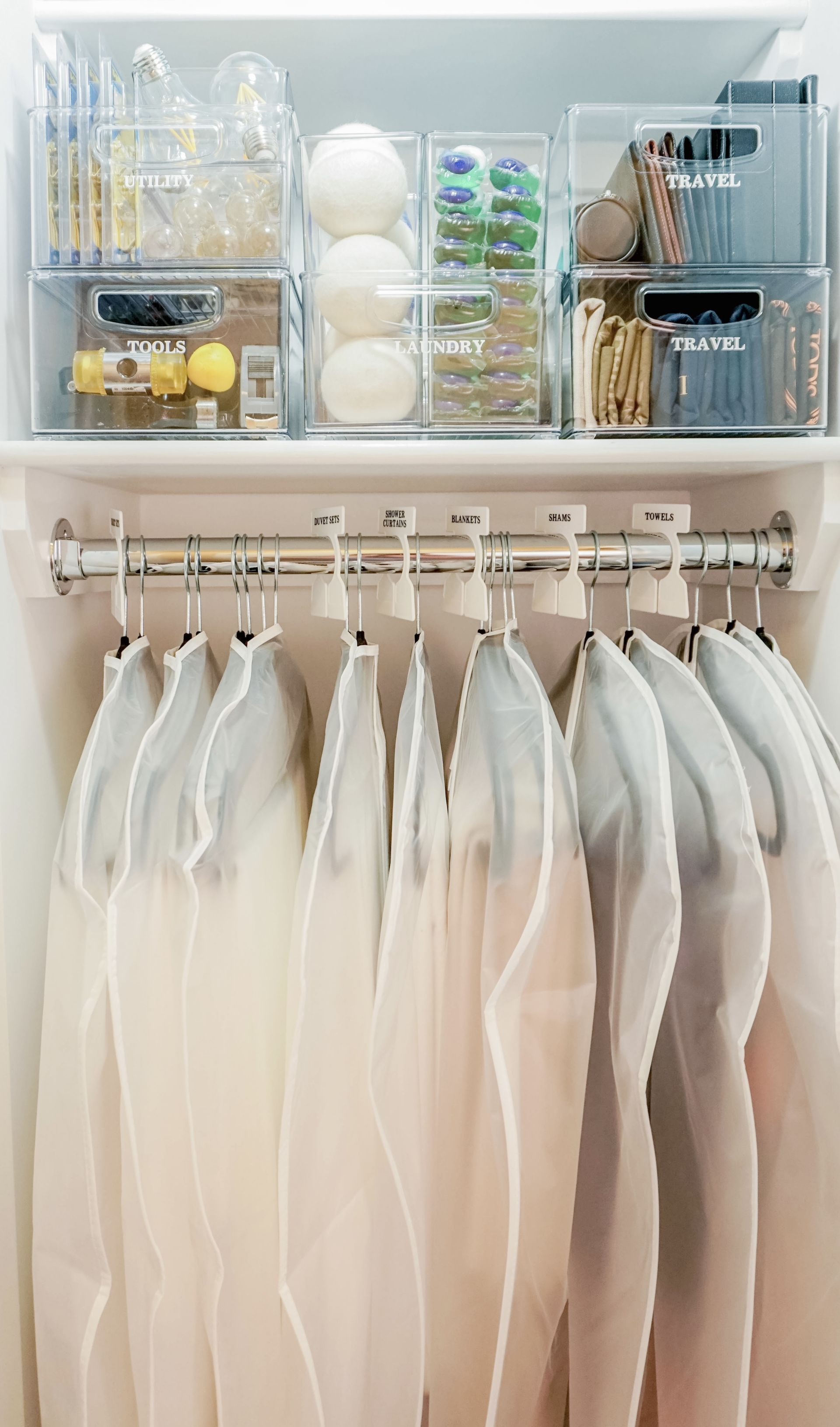 interior of hallway closet with hanging rail and labelled clear storage containers on shelf