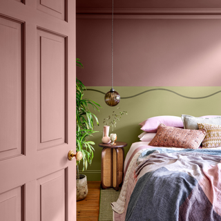 a painted bedroom wall of green and pink with a made double bed layered with bedding