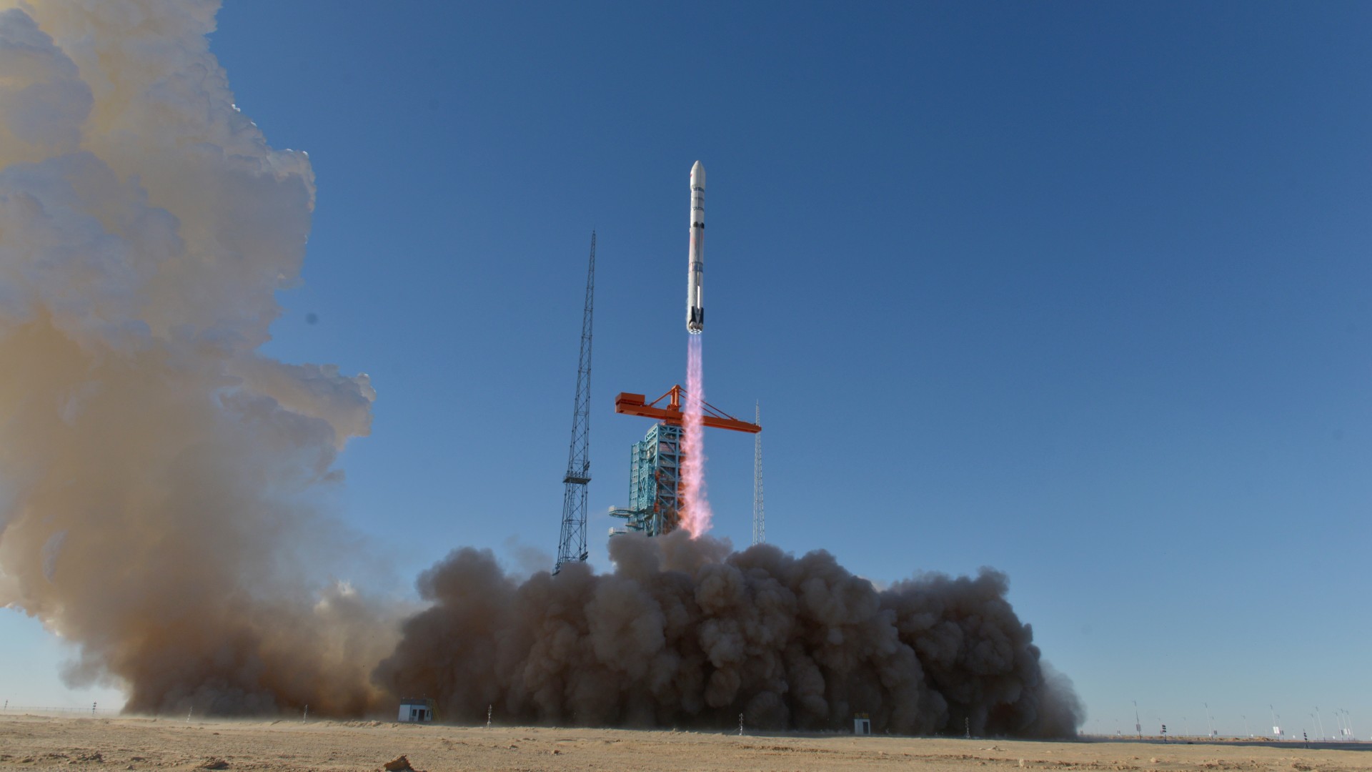 a white rocket lifts off above a cloud of dust and smoke in the desert