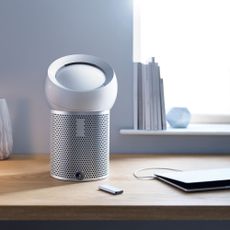 air purifier on a desk beside a window and a laptop