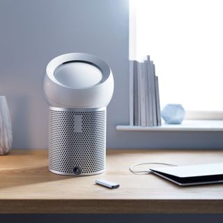 air purifier on a desk beside a window and a laptop
