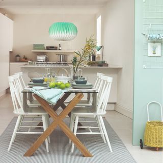 A kitchen with an adjoining dining area featuring a glass dining table with white chairs and a striped rug