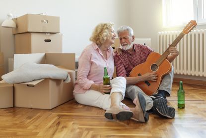 Happy Senior Couple Playing Guitar Together in New House Surrounded With Boxes After Moving