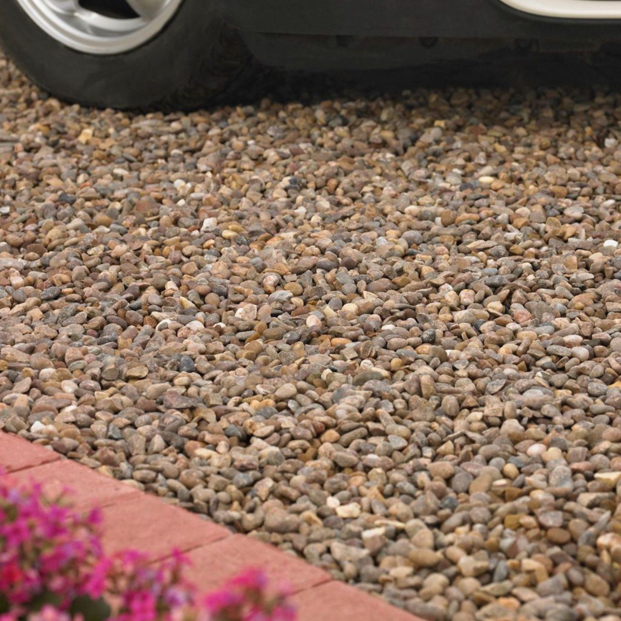 Detail of gravel driveway with car just seen and brick edging