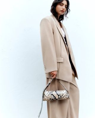 Woman wearing beige blazer, carrying snake print bag
