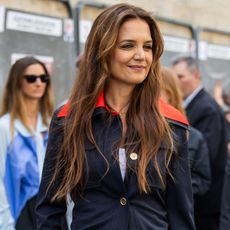 Katie Holmes smiles wearing a blue blazer with a red collar 