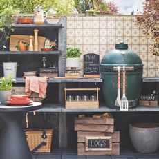 outdoor kitchen with tiled wall, big green egg BBQ, good storage, crates, side table, plates, log store, chopping boards