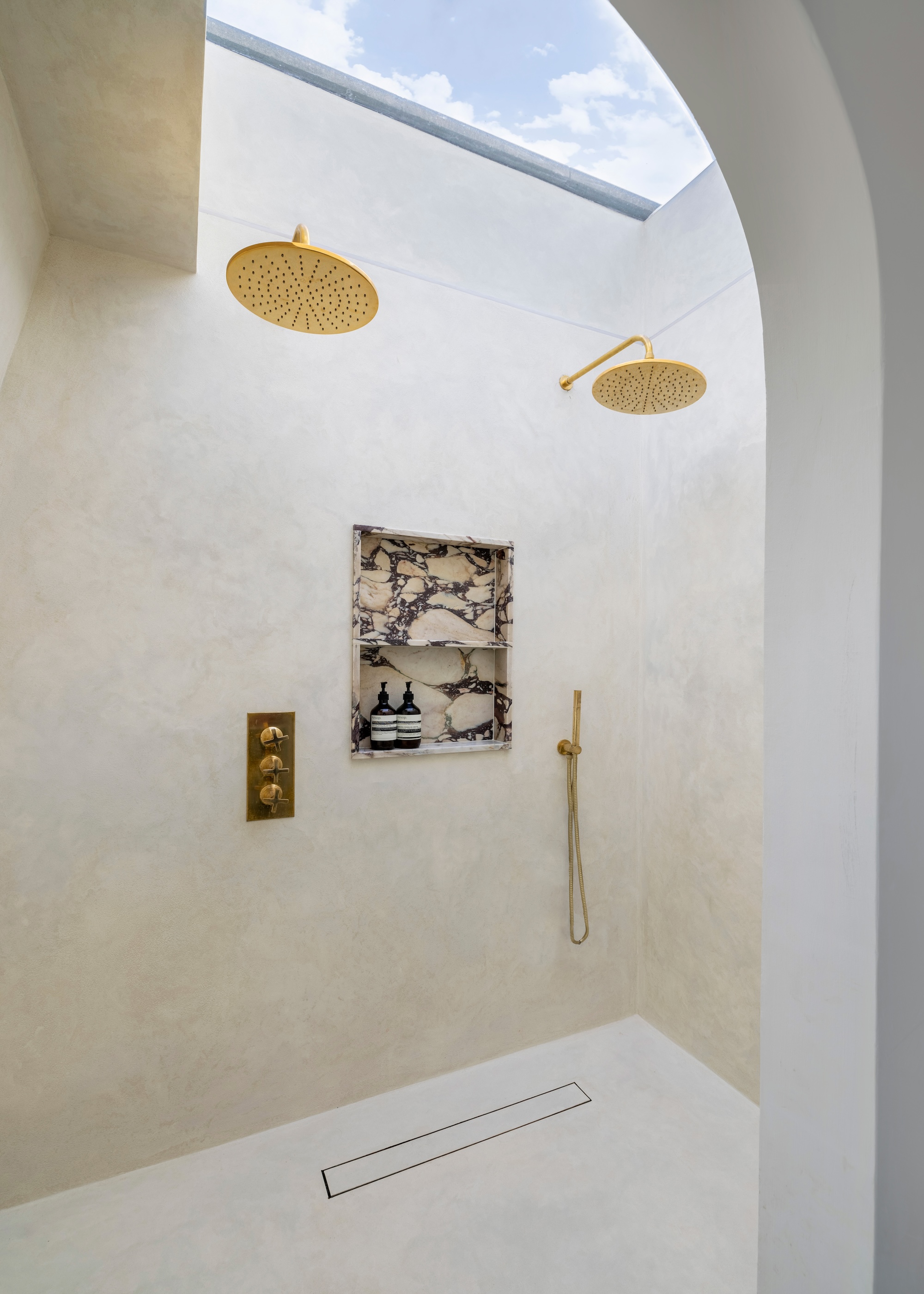 a generous walk in shower with two shower heads, a marble niche and a skylight letting natural light flood the space