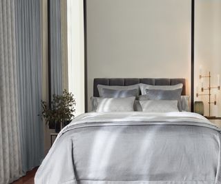 narrow rectangular mirrors hung vertically by side of bed with grey bedding and curtains