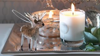 tray with scented candles burning and reindeer decoration to show how candles are an important christmas decorating idea