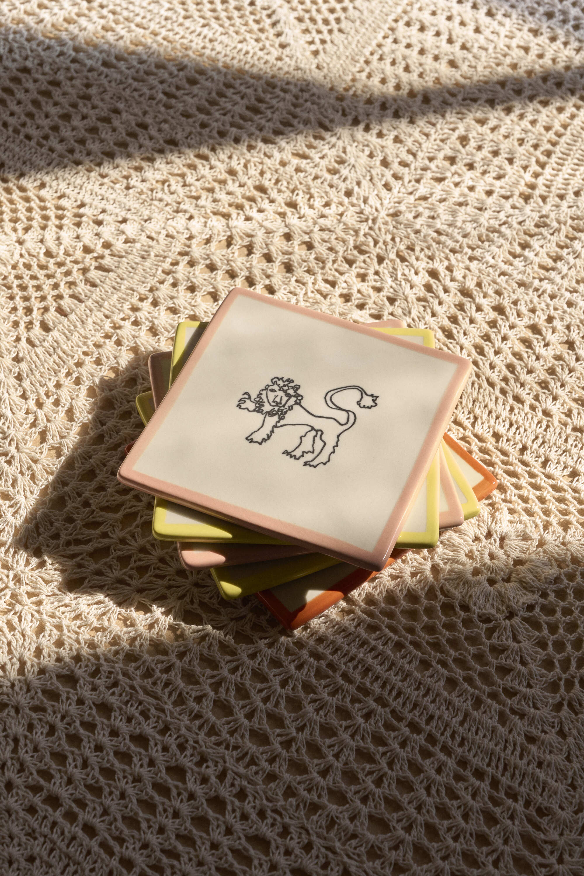 Close-up image of a crochet tablecloth with a stack of ceramic coasters with a lion illustration on them.