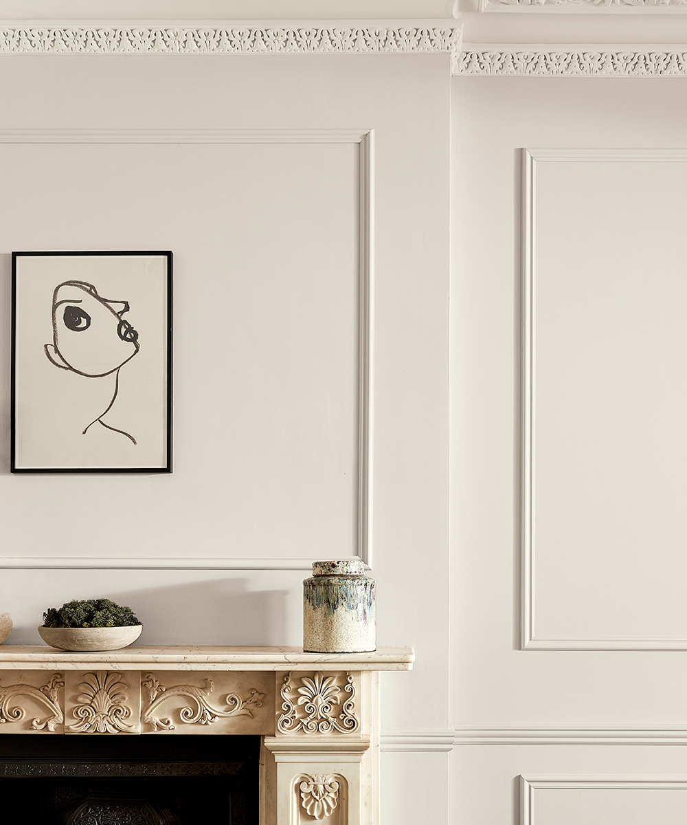 A white wall with an abstract painting above a white detailed fireplace