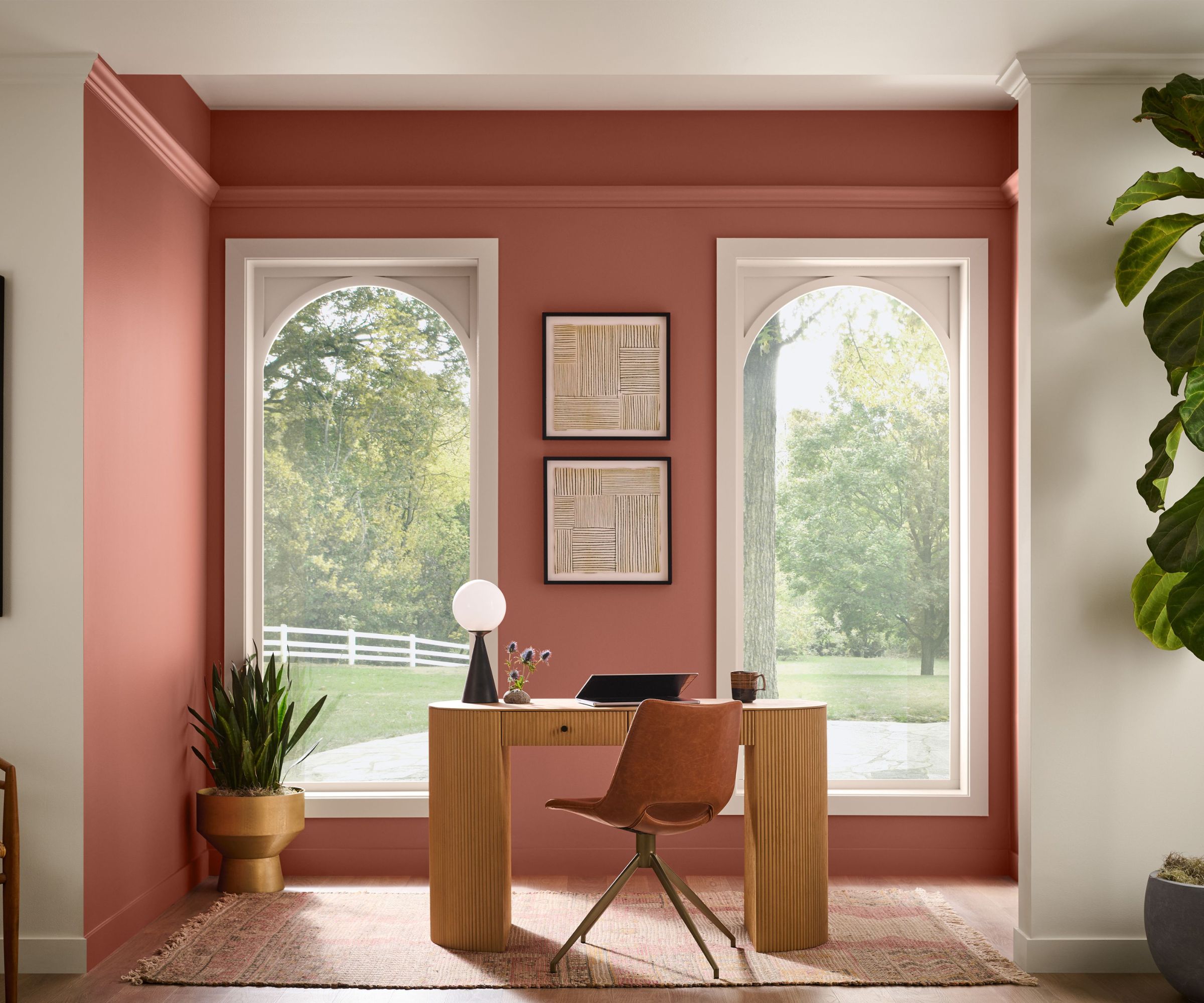 Office with large curved windows, wood desk and chair and terracotta painted wall