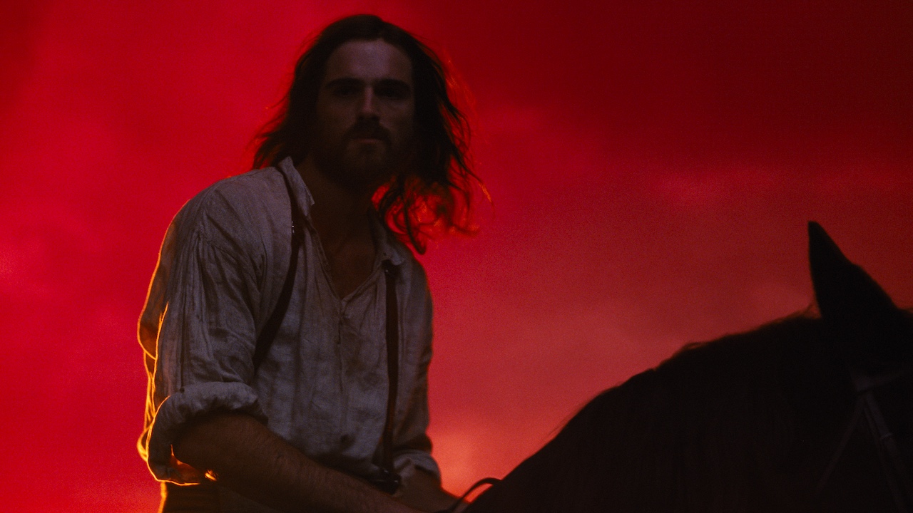 Jacob Elordi on a horse with red background in Wuthering Heights