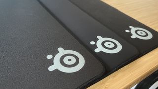 SteelSeries QcK Performance gaming mouse pad line on a wooden desk, with focus on brand logo