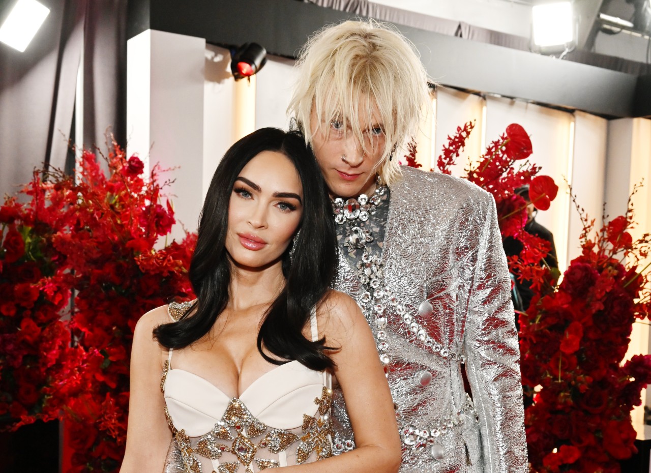 Megan Fox and Machine Gun Kelly standing together in shiny outfits.