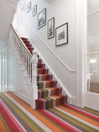 Hall and staircase with white walls and banister and striped carpet