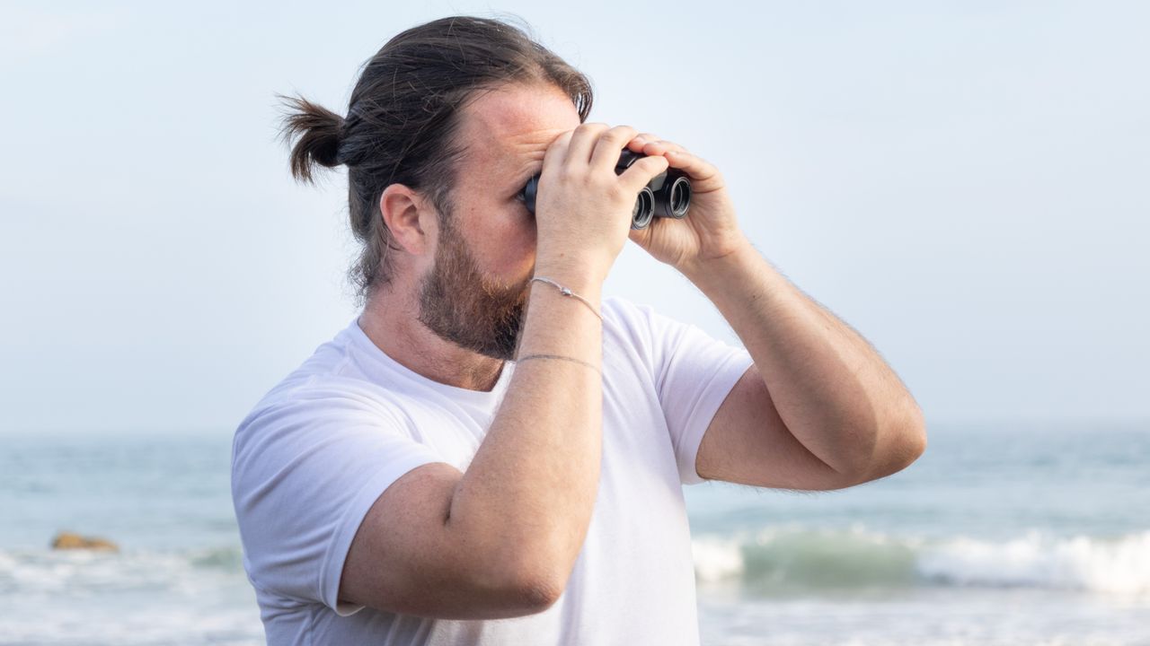 Nikon Stabilized 12x25 S binoculars held in the hands of the reviewer in front of breaking waves at the beach