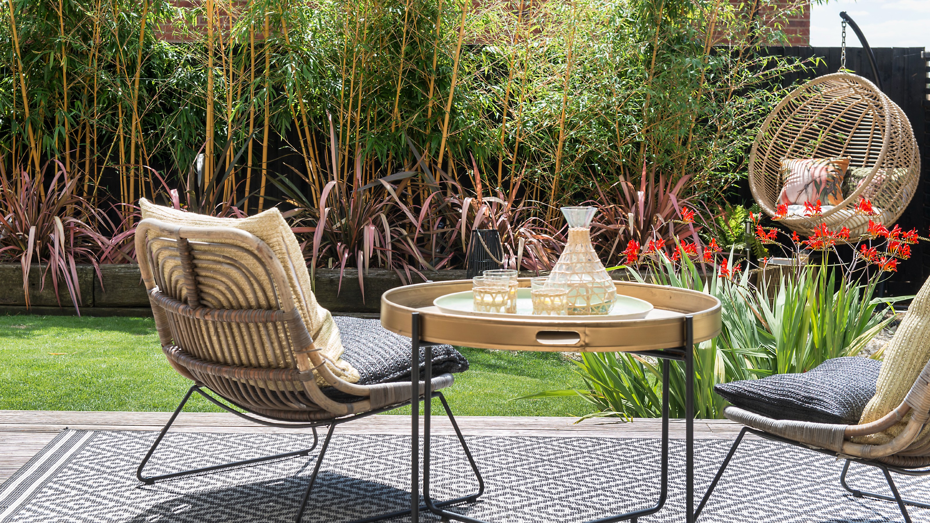 A garden with a set of two rattan chairs and a coffee table with a rattan egg chair to the side