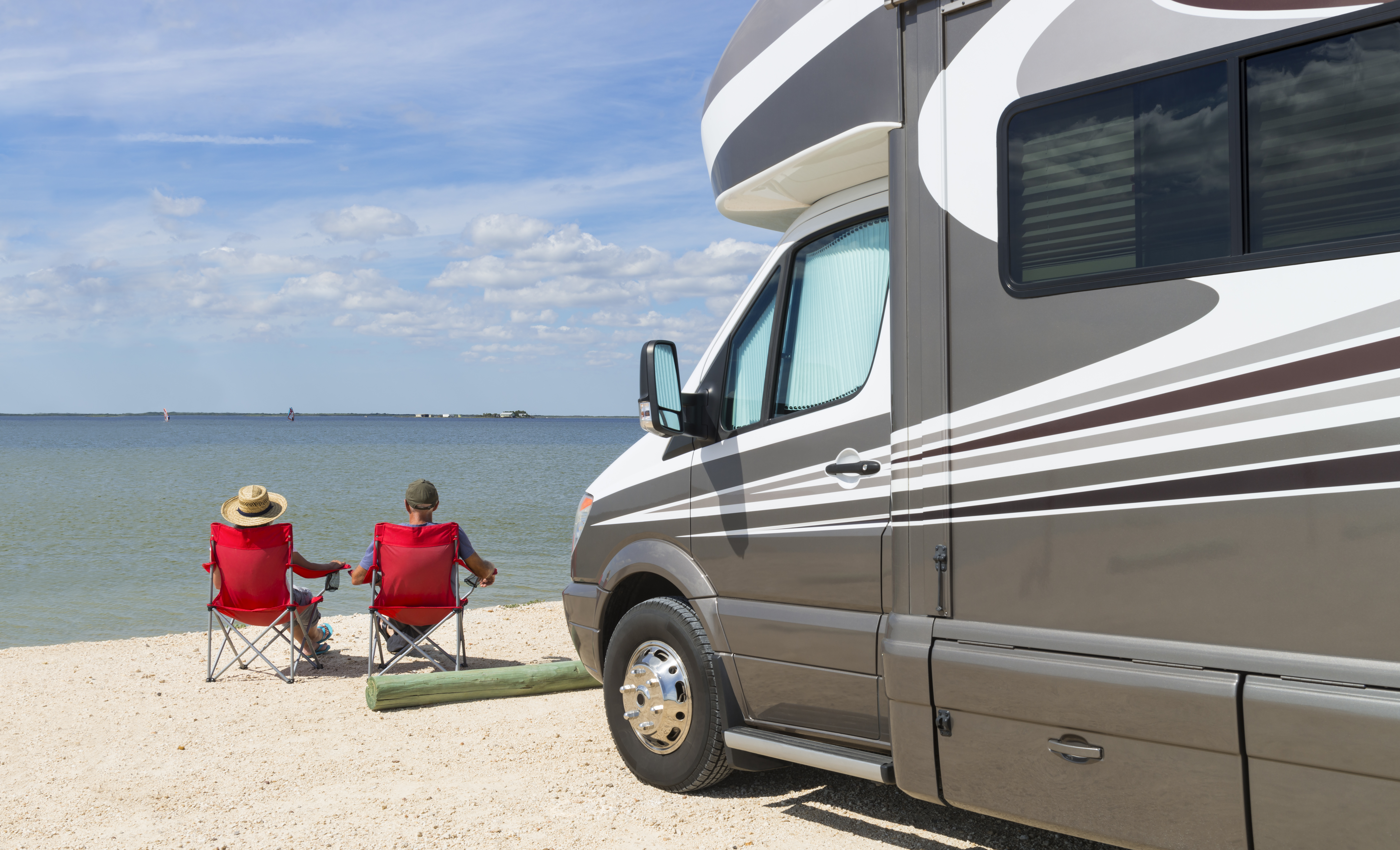 Senior couple sitting near water with motorhome in camping