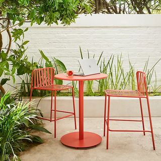 A red metal garden bar set with a laptop on the table