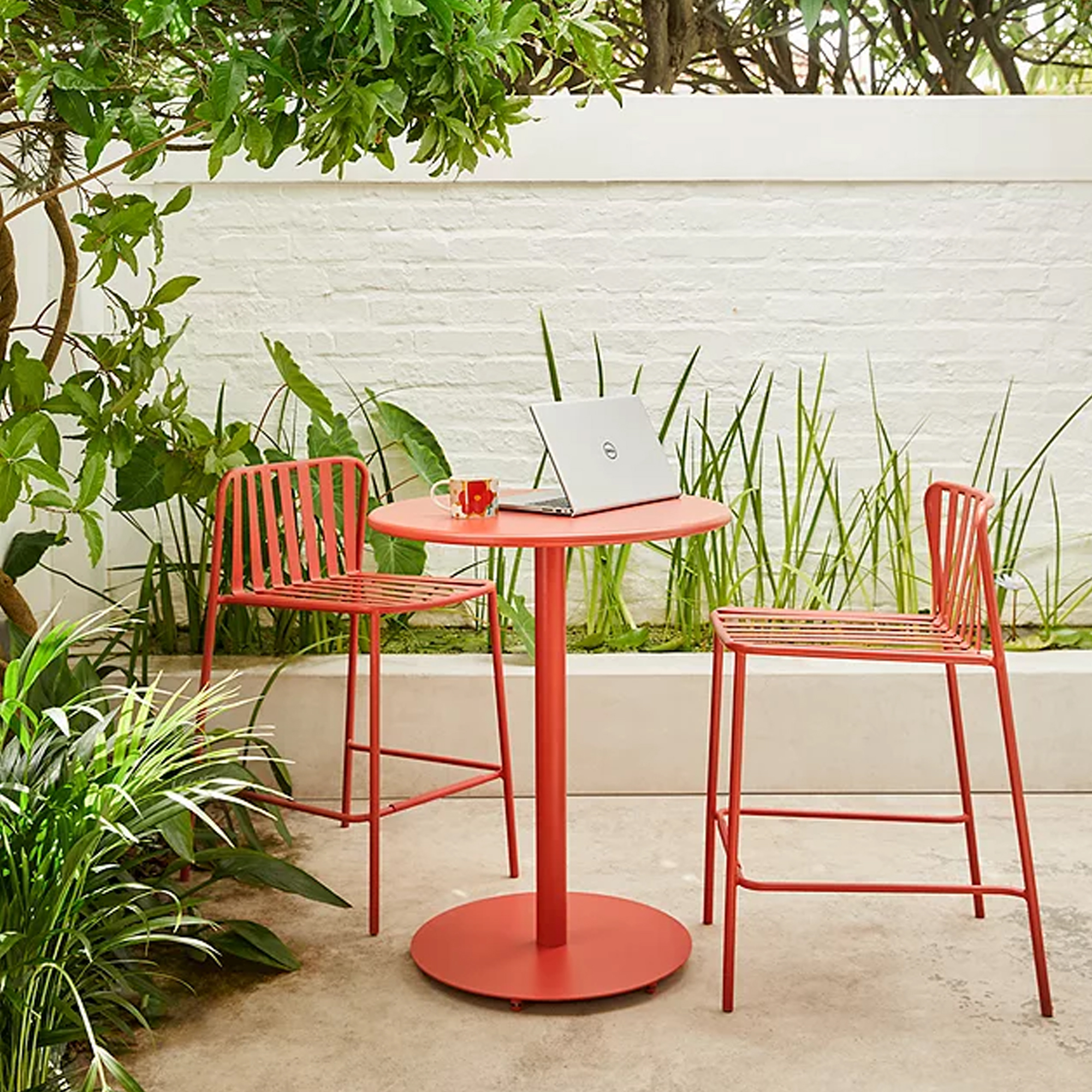 A red metal garden bar set with a laptop on the table