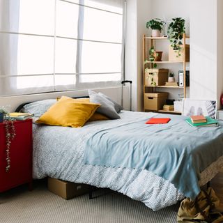 bed with blue comforter next to a red nightstand and a vertical shelf with books and baskets