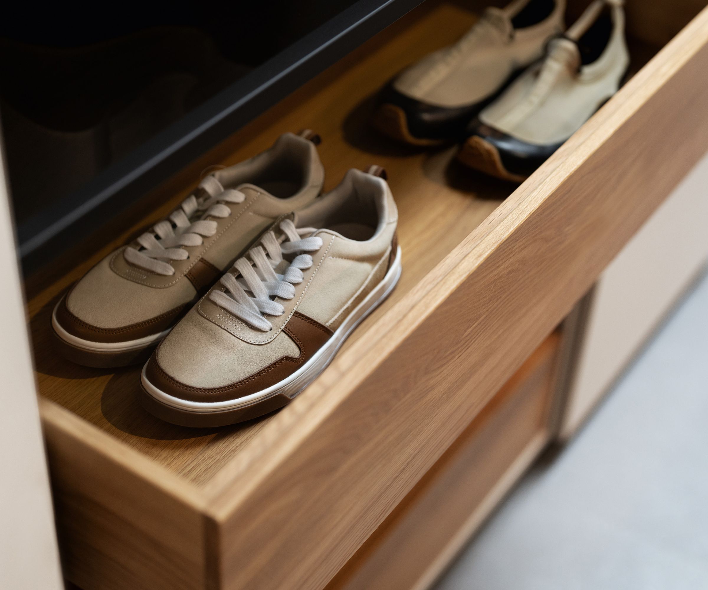 A natural wood drawer pulled out to reveal two pairs of trainers within. Both sets are beige, brown, black and white.