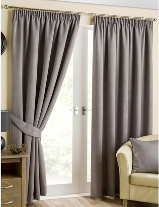 A living room with a cream sofa and Pewter Beaumont Blackout Pencil Pleat Curtains with one side pinned back revealing a door to outside