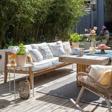 A garden with a wooden outdoor sofa with cream cushions and paired with a wooden coffee table