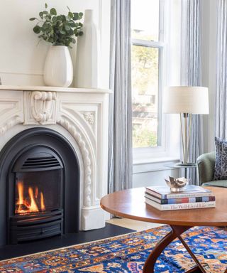 A brownstone living room with a molded fireplace, blue and orange area rug, and wooden coffee table