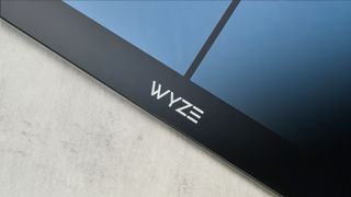 a close up picture of the wyze logo on a sleek, clean-looking smart scale with tempered glass finish and a cross-shaped design on top of the glass, almost blue in the studio lighting, rests upon a table