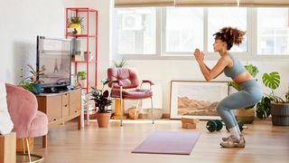 Woman going down into a squat in living room, watching workout video