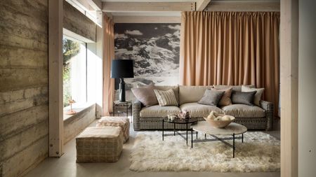 A modern statement living room with exposed wood panelling, a white fluffy rug, a brown sofa, statement wallpaper and peach colored curtain.