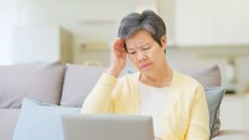 An older woman looking at her laptop in her living room looks distressed.
